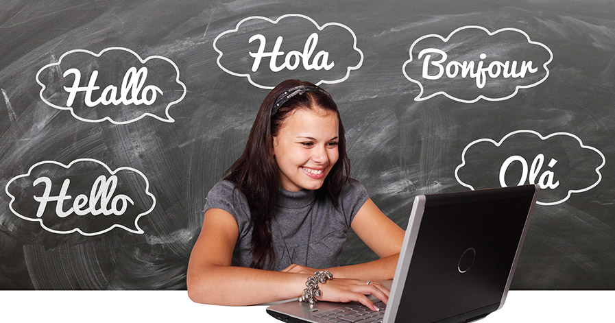 Young girl on laptop with "hello" in different languages on blackboard behind her