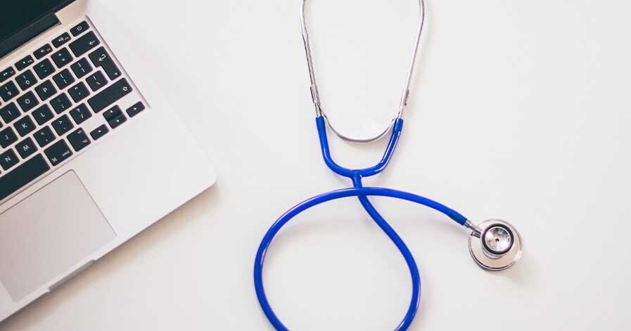 A photo of a stethoscope laying beside a laptop