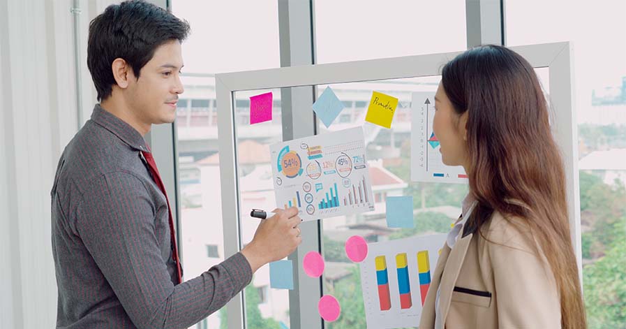 A scrum master going over information on a board with a company employee.